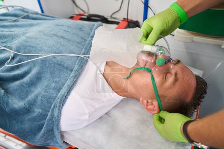 Foto de Paramédico pone máscara de oxígeno en el paciente en ambulancia, el médico trabaja en guantes de protección - Imagen libre de derechos