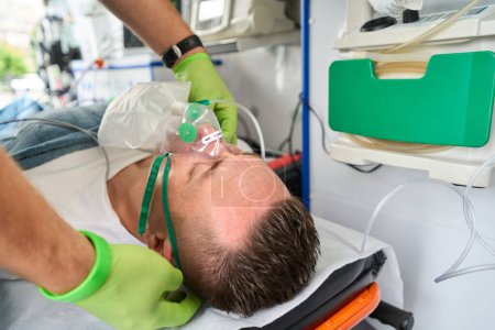 Foto de Médico del equipo móvil pone una máscara de oxígeno en un paciente en una ambulancia, un médico usa guantes protectores - Imagen libre de derechos