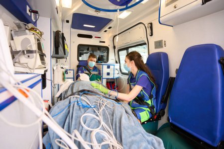Foto de Médicos del equipo móvil transportan al paciente en una ambulancia, el médico rellena el cuestionario de pacientes - Imagen libre de derechos