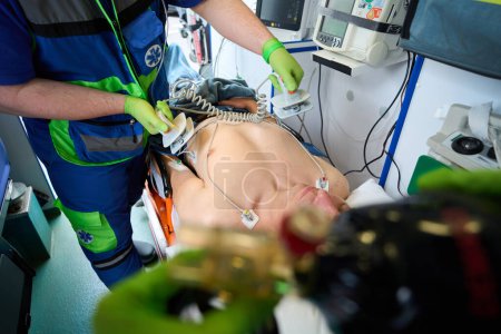 Photo for Fellow paramedics resuscitate an injured man in an ambulance, using a defibrillator and a breathing bag - Royalty Free Image