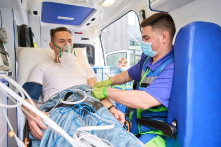 Photo for Paramedic administering medicine to a patient in an ambulance, an injured person wearing an oxygen mask - Royalty Free Image