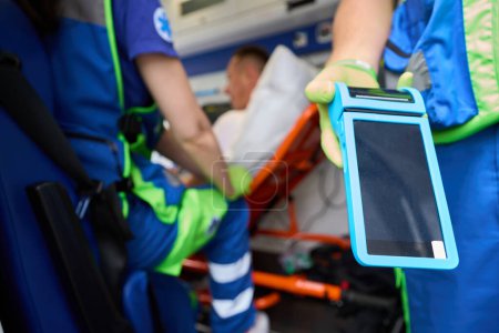 Téléchargez les photos : Le médecin de l'équipe visiteuse tient un appareil médical dans ses mains, à côté de son collègue et d'un patient sur une civière - en image libre de droit