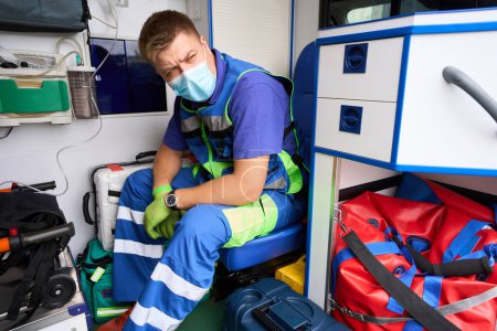 Photo for Paramedic in a protective mask is in an ambulance, the car has modern equipment - Royalty Free Image