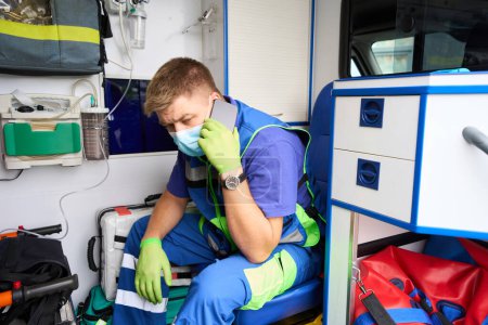 Foto de El médico del equipo que visita comunica en un teléfono móvil en una ambulancia, el coche tiene equipo moderno - Imagen libre de derechos