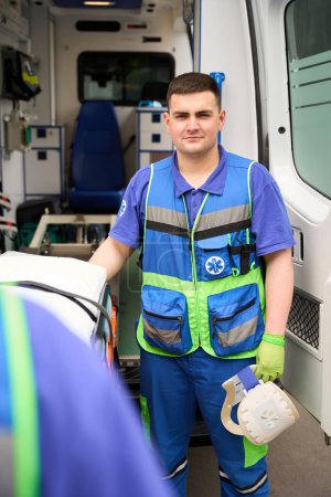 Photo for Paramedic holds a neck brace in his hands to fix and support the patients cervical vertebrae, next to the ambulance - Royalty Free Image