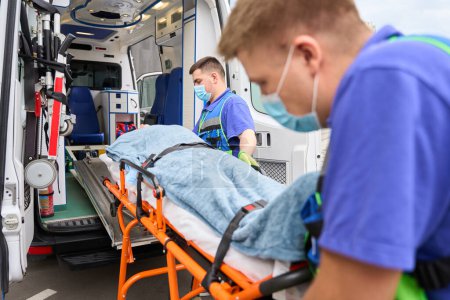 Foto de Hombres colegas paramédicos descargar una camilla con una víctima de una ambulancia, en el coche hay equipos modernos - Imagen libre de derechos