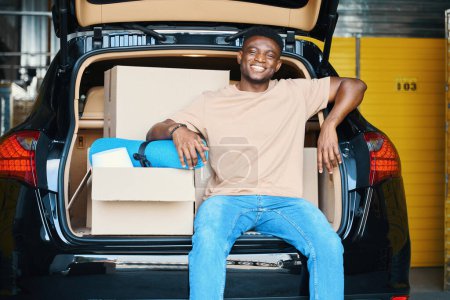 Foto de El joven afroamericano está descansando en el maletero de un auto, trajo cosas para almacenarlas al servicio - Imagen libre de derechos