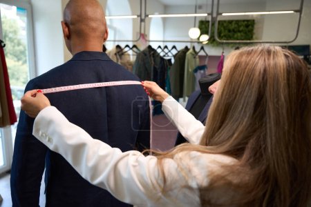 Téléchargez les photos : Couturière expérimentée mesurant la largeur des épaules d'un homme adulte avec ruban à mesurer en atelier - en image libre de droit