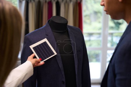 Foto de Foto recortada del diseñador de moda adjuntando una muestra para adaptarse a la chaqueta en el maniquí en presencia de un colega - Imagen libre de derechos