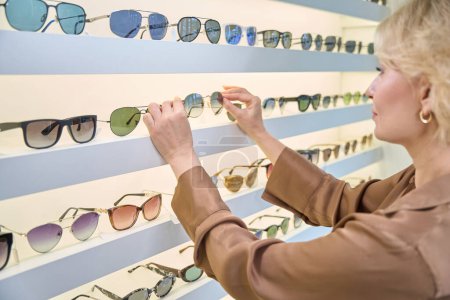 Foto de Señora en una blusa marrón elige gafas de sol, hay una amplia selección de gafas en exhibición - Imagen libre de derechos