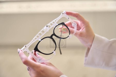 Foto de Oftalmólogo sostiene gafas y un aparato oftálmico en sus manos, un especialista en su lugar de trabajo en un salón de óptica - Imagen libre de derechos