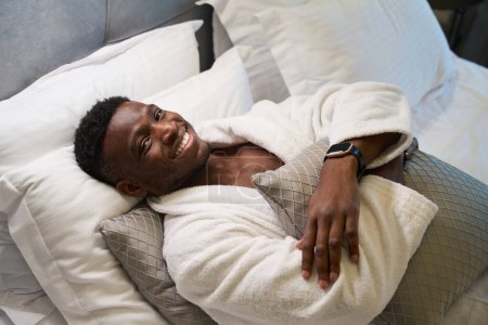 Foto de Hombre disfruta de la relajación de la mañana en un acogedor dormitorio, él está en un albornoz suave - Imagen libre de derechos
