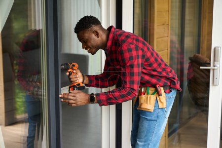 Foto de Reparador afroamericano repara una puerta de cristal, usa un destornillador - Imagen libre de derechos