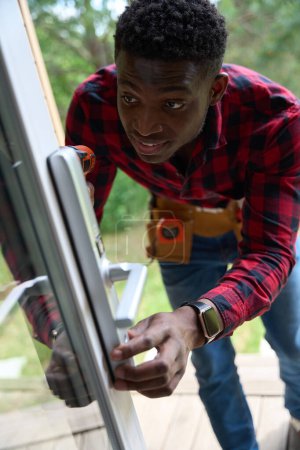 Foto de Reparador de pelo rizado repara una puerta de vidrio, utiliza un destornillador - Imagen libre de derechos