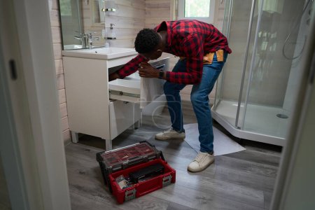Téléchargez les photos : Travailleur afro-américain fait des rénovations mineures salle de bains en utilisant sa trousse à outils - en image libre de droit