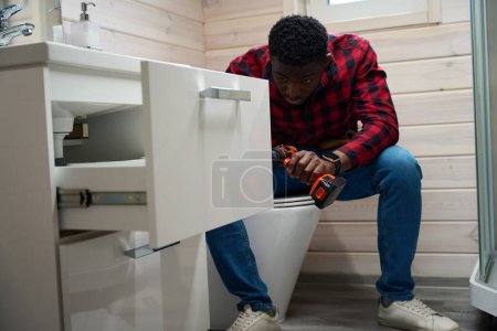 Téléchargez les photos : Homme travailleur fait des rénovations mineures dans la salle de bain, il utilise sa trousse à outils - en image libre de droit