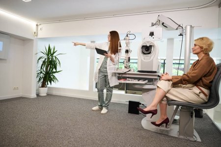 Foto de Consultor oftalmólogo comprueba la visión de un paciente, las mujeres se encuentran en un consultorio luminoso - Imagen libre de derechos