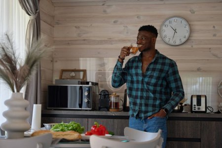 Foto de Hombre afroamericano bebe té en una acogedora cocina, la habitación es limpia y luminosa - Imagen libre de derechos