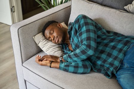Photo for Young guy fell asleep on a cozy sofa, wearing a plaid shirt and jeans - Royalty Free Image