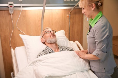 Téléchargez les photos : Infirmière expérimentée s'occupe d'un patient âgé, l'homme repose sur un lit mobile spécial - en image libre de droit