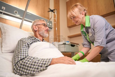 Téléchargez les photos : Jeune infirmière donne une injection dans une veine d'un homme âgé, le patient s'allonge sur un lit mobile spécial - en image libre de droit
