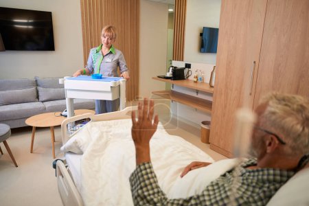 Téléchargez les photos : Une patiente âgée accueille une bonne infirmière, une femme est entrée dans la pièce avec une table d'injection - en image libre de droit