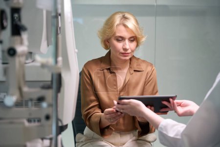 Foto de Médico femenino consultando señora de mediana edad, dispositivos profesionales modernos en interiores - Imagen libre de derechos