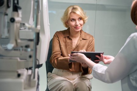 Téléchargez les photos : L'ophtalmologiste féminine consulte une femme d'âge moyen, la patiente signe un contrat - en image libre de droit