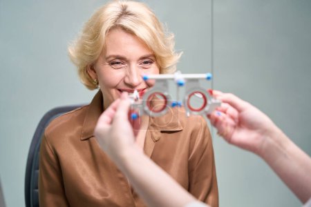 Foto de El doctor se pone un dispositivo especial para diagnosticar los ojos de una mujer, una dama con una blusa marrón - Imagen libre de derechos