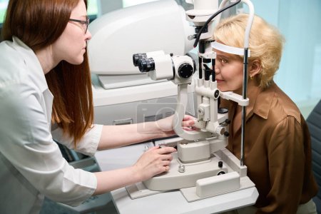 Photo for Ophthalmologist uses a modern dioptrimeter in his work, the client sits opposite the machine - Royalty Free Image