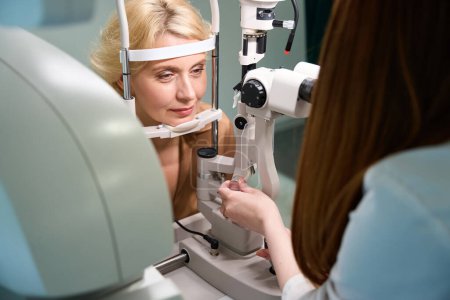 Foto de Hermosa mujer en una cita con un oftalmólogo, un especialista utiliza un dispositivo moderno en el trabajo - Imagen libre de derechos