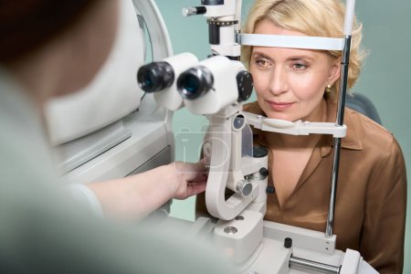 Téléchargez les photos : Élégante dame à un rendez-vous chez l'ophtalmologiste, le médecin utilise un appareil moderne au travail - en image libre de droit