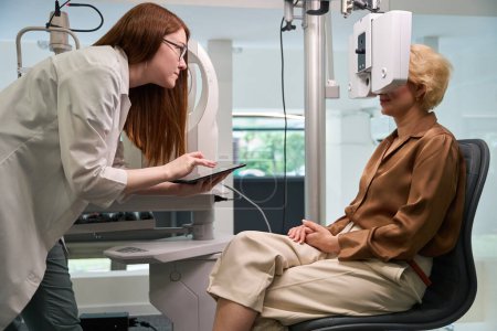 Téléchargez les photos : L'ophtalmologiste féminine utilise un dioptéromètre dans son travail, le client est assis près de l'appareil - en image libre de droit