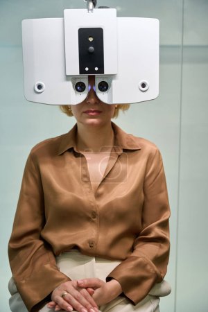 Foto de Paciente en una blusa marrón se somete a un examen oftalmológico, un dispositivo moderno se utiliza en una cita con un oftalmólogo - Imagen libre de derechos