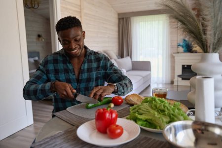 Téléchargez les photos : Heureux homme afro-américain préparant une salade de légumes juteux, il est dans des vêtements décontractés confortables - en image libre de droit