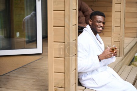 Téléchargez les photos : Gentil gars sur la véranda avec le thé du matin, il est dans un confortable peignoir éponge - en image libre de droit