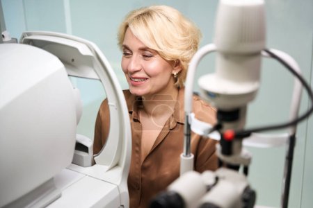 Smiling woman sits in front of a special ophthalmic device, a lady at an appointment with a specialist