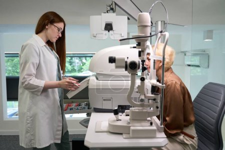 Foto de Joven médico examina los ojos de una señora de mediana edad, dispositivos oftalmológicos modernos en el interior - Imagen libre de derechos