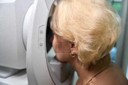Foto de Rubia se sienta frente a un dispositivo oftálmico especial, una dama en una cita con un oftalmólogo - Imagen libre de derechos