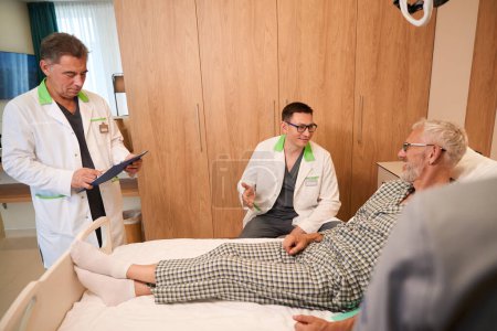 Téléchargez les photos : Homme âgé souriant communique avec les médecins en salle, intérieur minimaliste intérieur - en image libre de droit