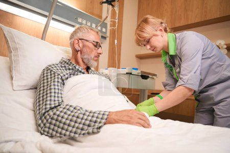 Téléchargez les photos : Infirmière donne une injection dans une veine d'un vieil homme barbu, le patient s'allonge sur un lit mobile spécial - en image libre de droit