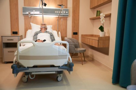Téléchargez les photos : L'homme âgé se trouve sur un lit mobile spécial, il est traité dans un établissement médical moderne - en image libre de droit
