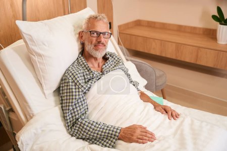 Téléchargez les photos : Vieil homme reçoit une IV dans un établissement médical moderne, la chambre est lumineuse et propre - en image libre de droit