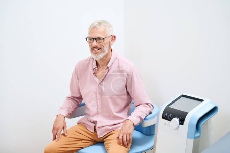 Téléchargez les photos : Vieil homme subissant une procédure de physiothérapie pour stimuler les muscles du plancher pelvien, la clinique dispose d'équipements modernes - en image libre de droit