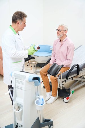 Photo for Medical worker introduces a patient to a device for physiotherapy to stimulate the muscles of the penis and prostate - Royalty Free Image