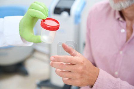 Téléchargez les photos : Un assistant de laboratoire donne à un homme un récipient pour recueillir un test d'urine, un médecin travaille dans des gants de protection - en image libre de droit