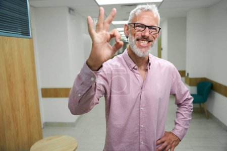 Photo for Bearded man in a pink shirt shows ok, the hospital corridor is empty and clean - Royalty Free Image