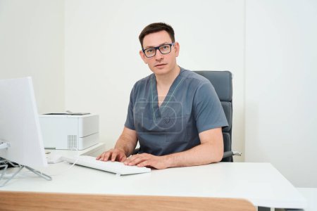 Téléchargez les photos : Médecin travaille à un ordinateur sur le lieu de travail, il y a de l'équipement moderne dans le bureau - en image libre de droit