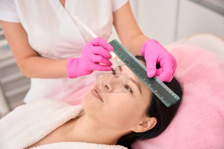 Photo for Esthetician marks the clients eyebrows before the procedure, the master uses a special pencil and ruler - Royalty Free Image