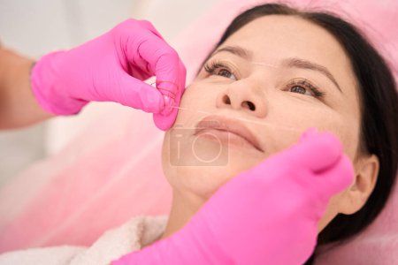 Foto de Médico esteticista marca los labios de los clientes antes del procedimiento con un hilo especial, el maestro trabaja en guantes de protección - Imagen libre de derechos